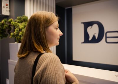 A woman waiting at the dental clinic reception, viewed from the side. Indoor setting.